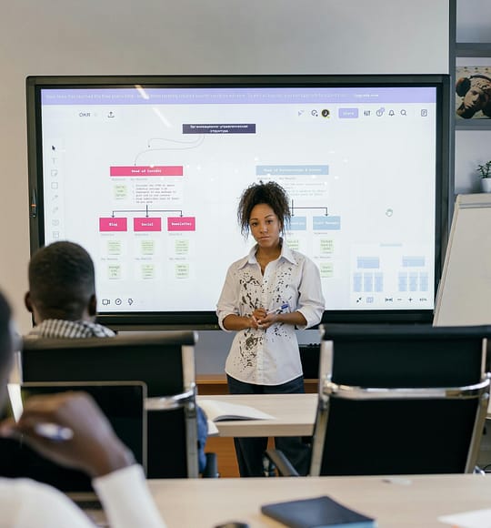 A professional business woman leads a meeting with a diverse team, using a digital display.