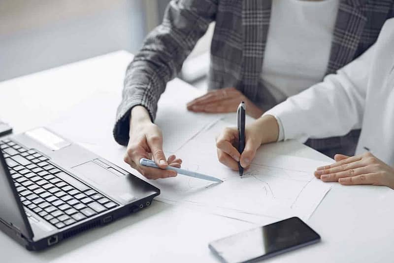 person is holding a pen and the other is pointing at the paper with the ruler